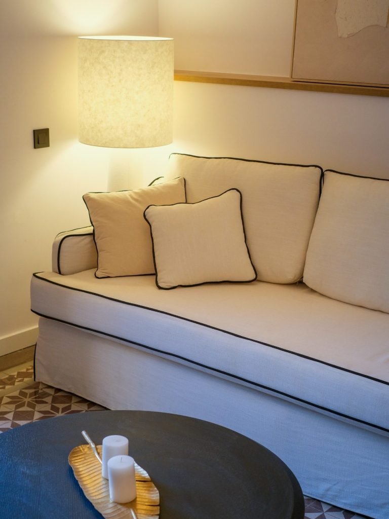 Sofá blanco con cojines, lámpara de luz suave y mesa de centro de madera.