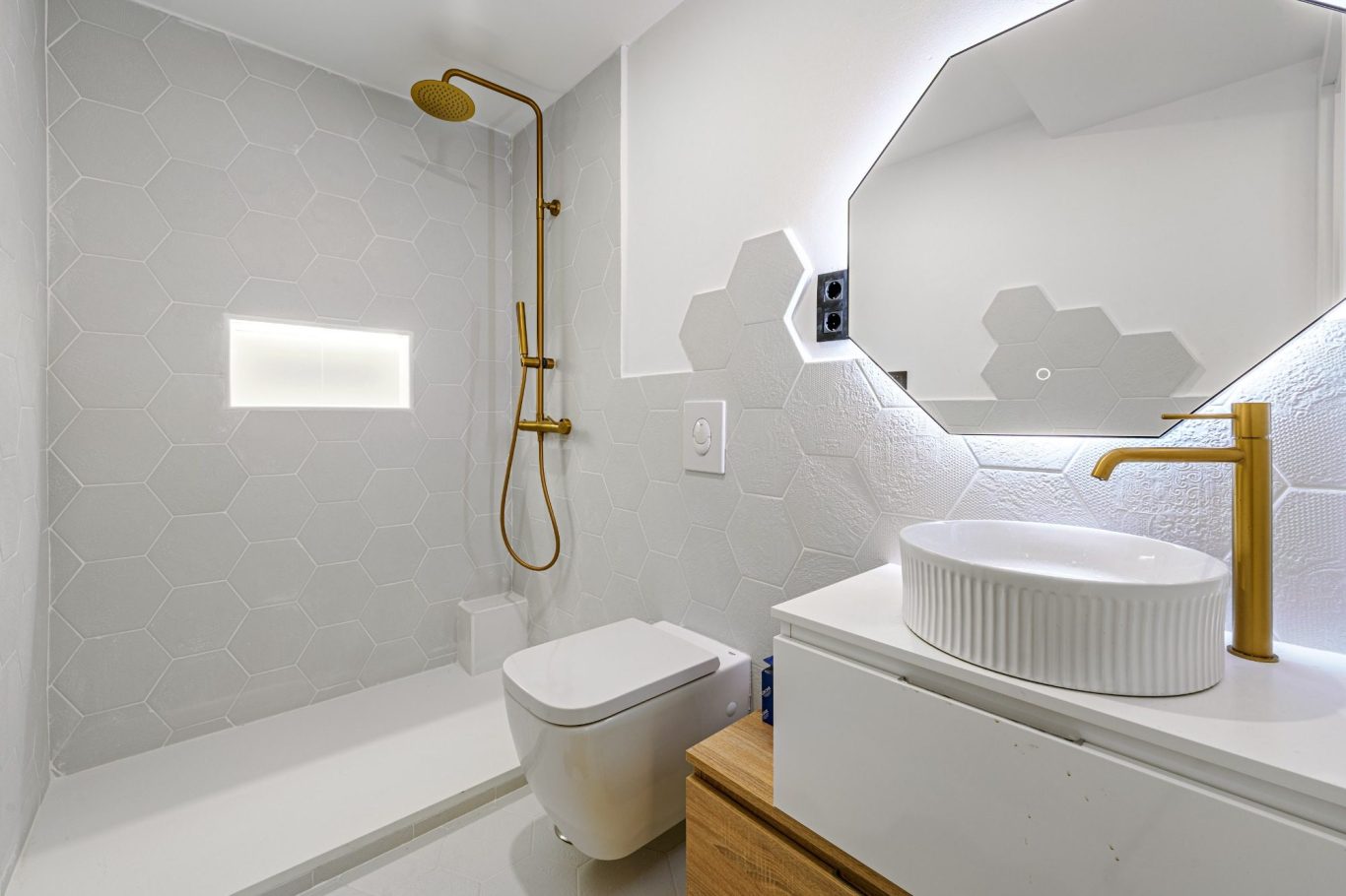 Baño moderno con ducha, lavabo circular, y grifería dorada sobre fondo blanco.