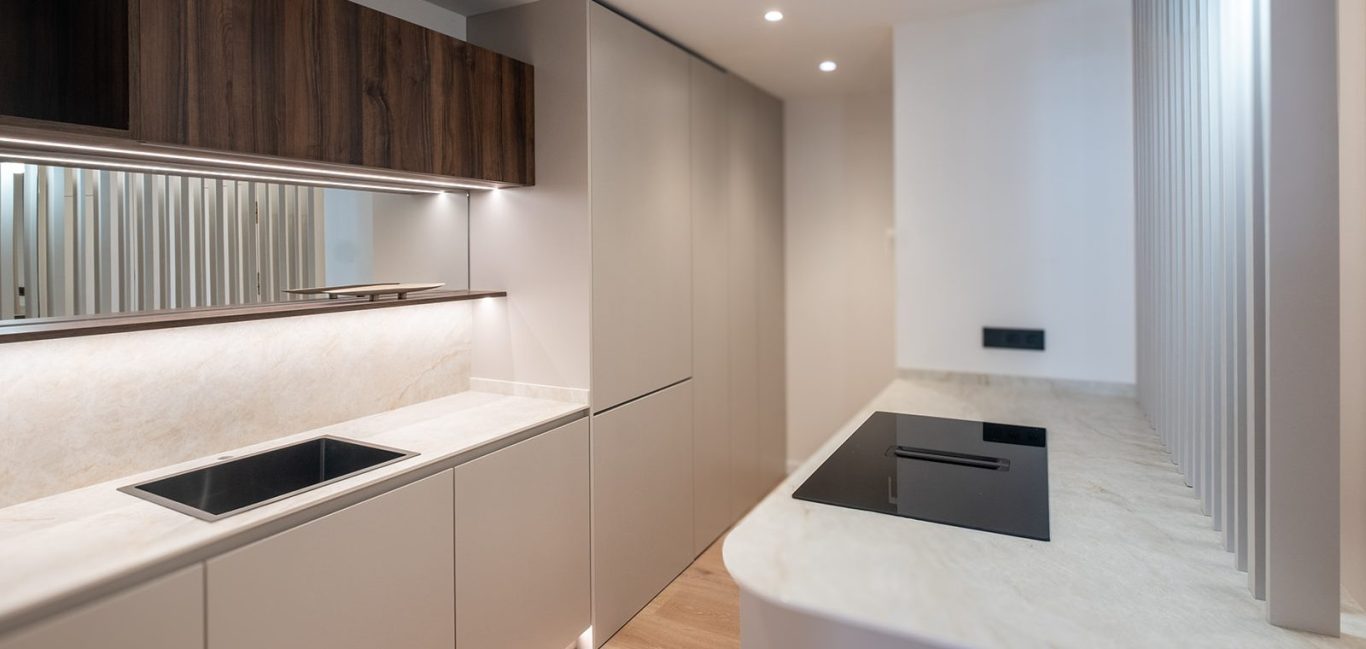 Cocina moderna con encimera blanca y paredes en tonos claros. Detalles en madera oscura.