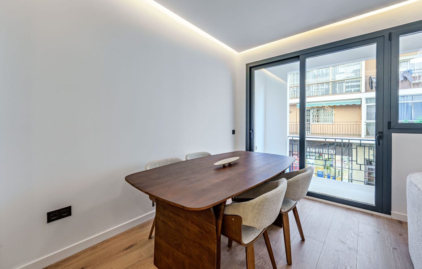 Mesa de madera con sillas en un ambiente luminoso, junto a una ventana.