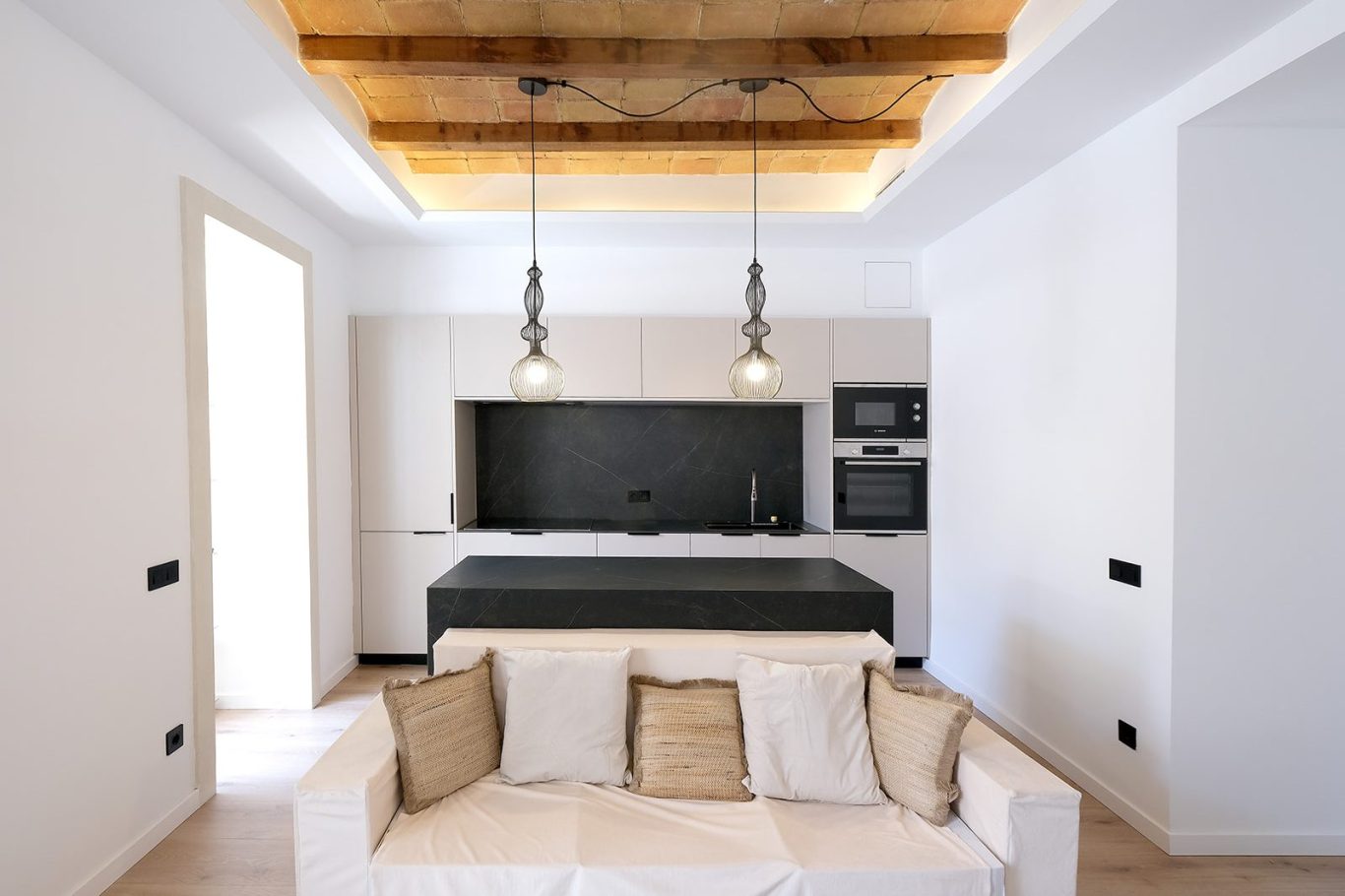 Sala de estar moderna con cocina abierta y techos de madera. Sofá claro y detalles minimalistas.