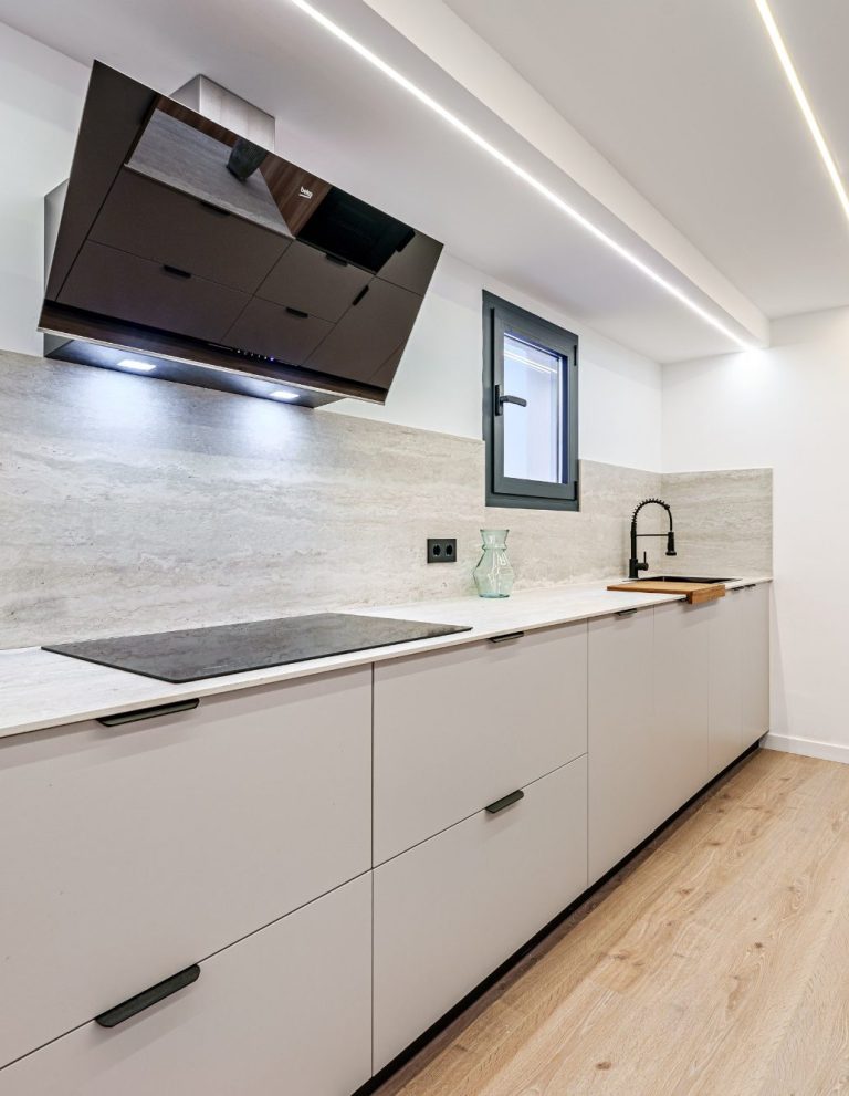 Cocina moderna con armarios grises, una campana extractora y encimera clara.