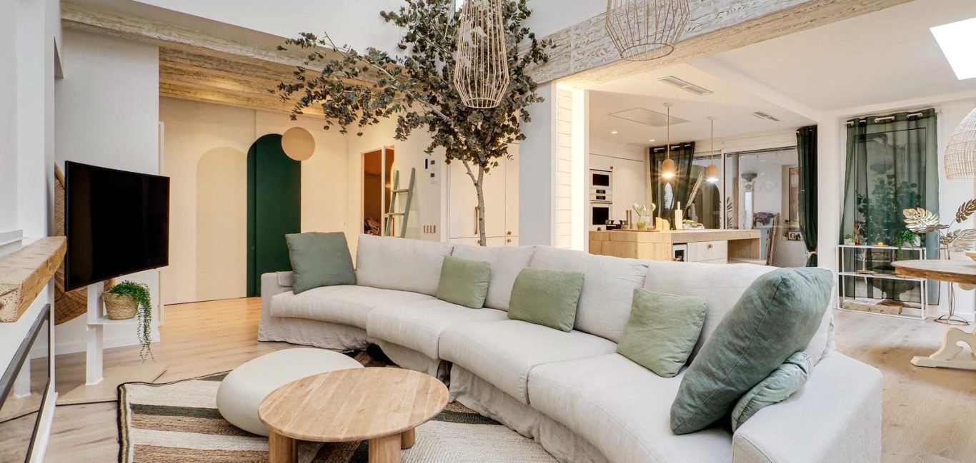 Interior luminoso con techos altos, muebles modernos y un jardín visible a través de las ventanas.