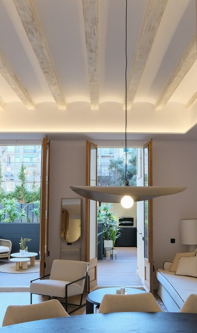 Interior luminoso con techos altos, muebles modernos y un jardín visible a través de las ventanas.