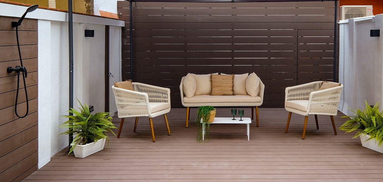 Zona de estar al aire libre con sofá y sillas de mimbre, decorada con plantas.