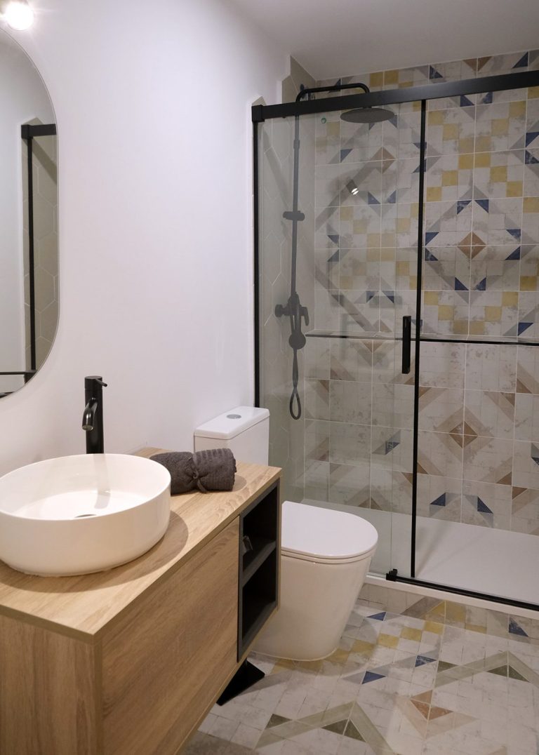 Baño moderno con lavabo redondo, ducha con mampara y azulejos decorativos.