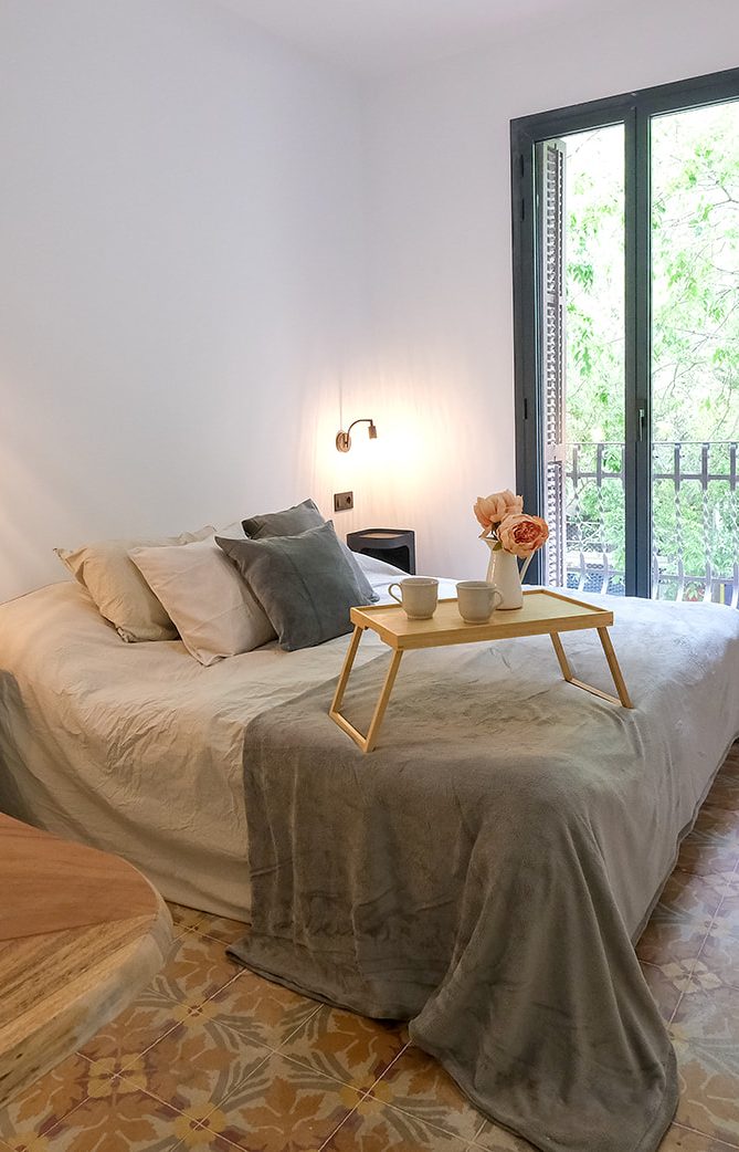 Habitación acogedora con cama grande, mesa con flores y ventanal iluminado.