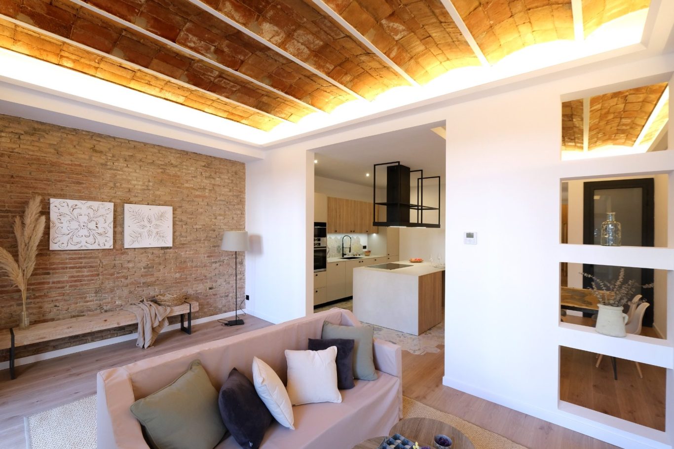 Sala de estar moderna con sofá, lámparas y cocina al fondo. Pared de ladrillo vista.