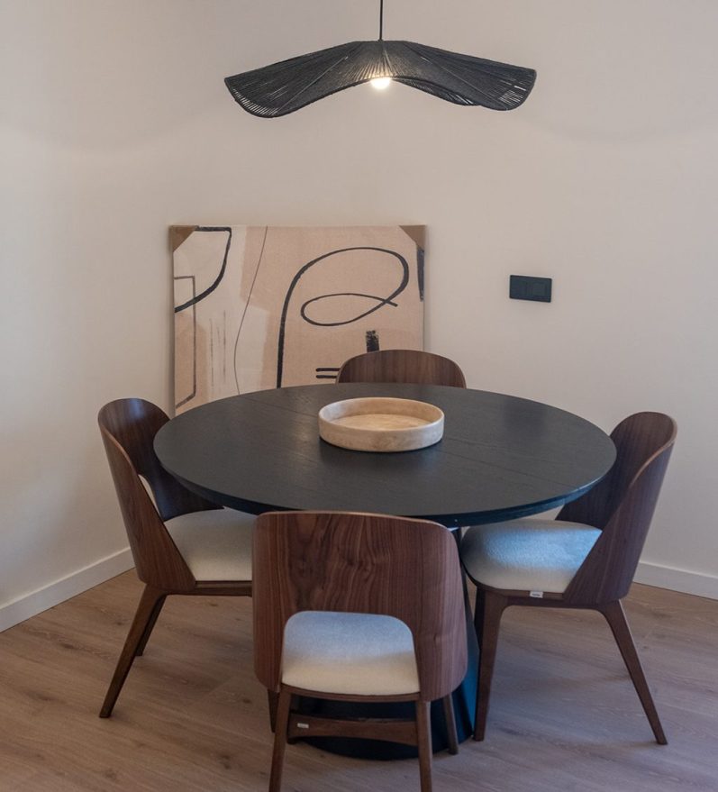 Mesa redonda negra con sillas marrones y una lámpara colgante sobre ella.