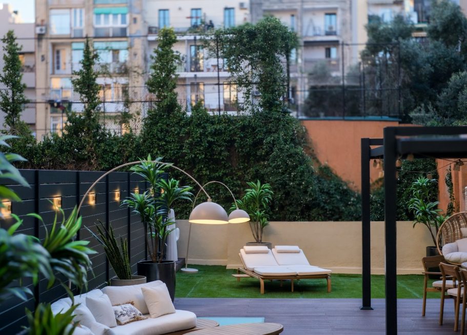 Jardín moderno con tumbonas, plantas y mobiliario en un ambiente urbano.