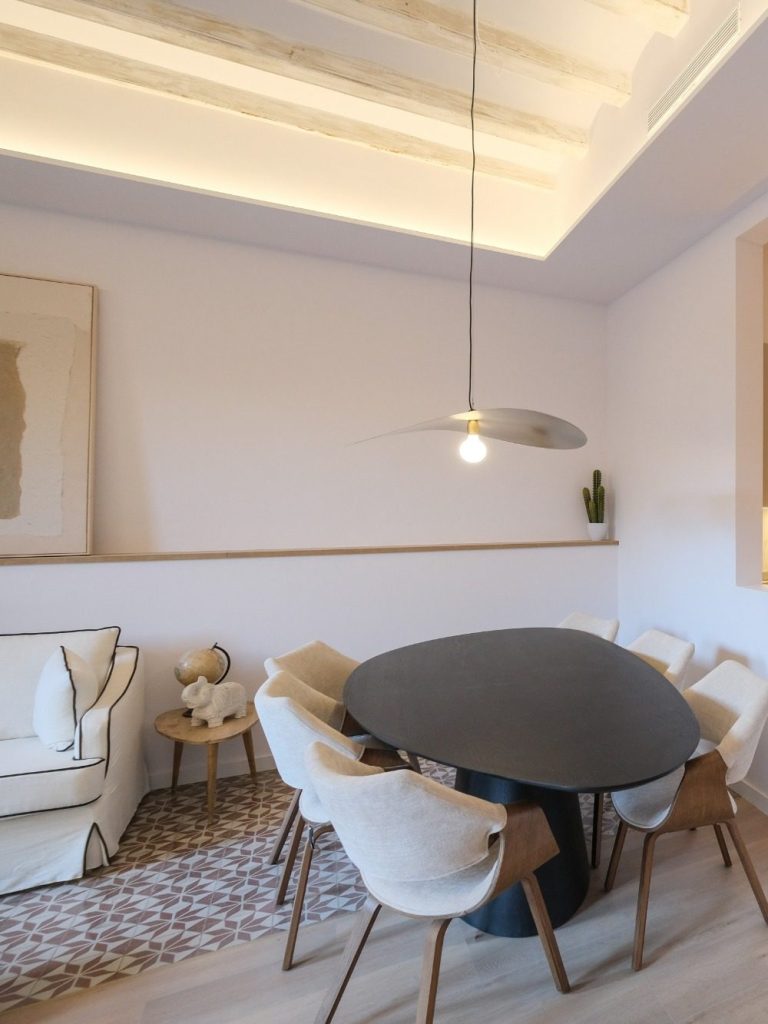 Sala comedor moderna con mesa negra y sillas blancas, iluminada con luz suave.