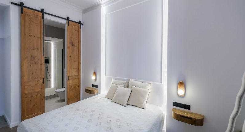 Habitación moderna con cama doble, paneles de madera y luz suave en las paredes.