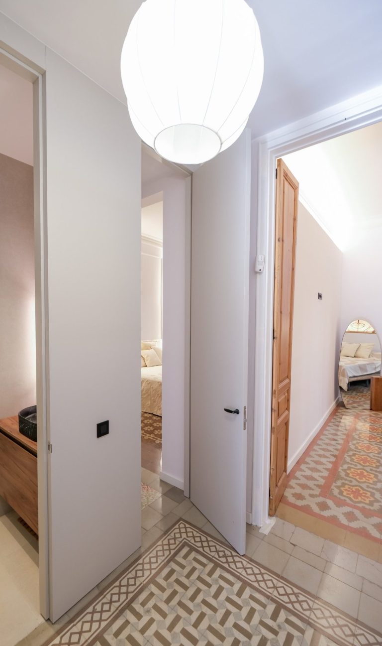 Puerta abierta hacia una habitación iluminada con lámpara y suelo decorativo.