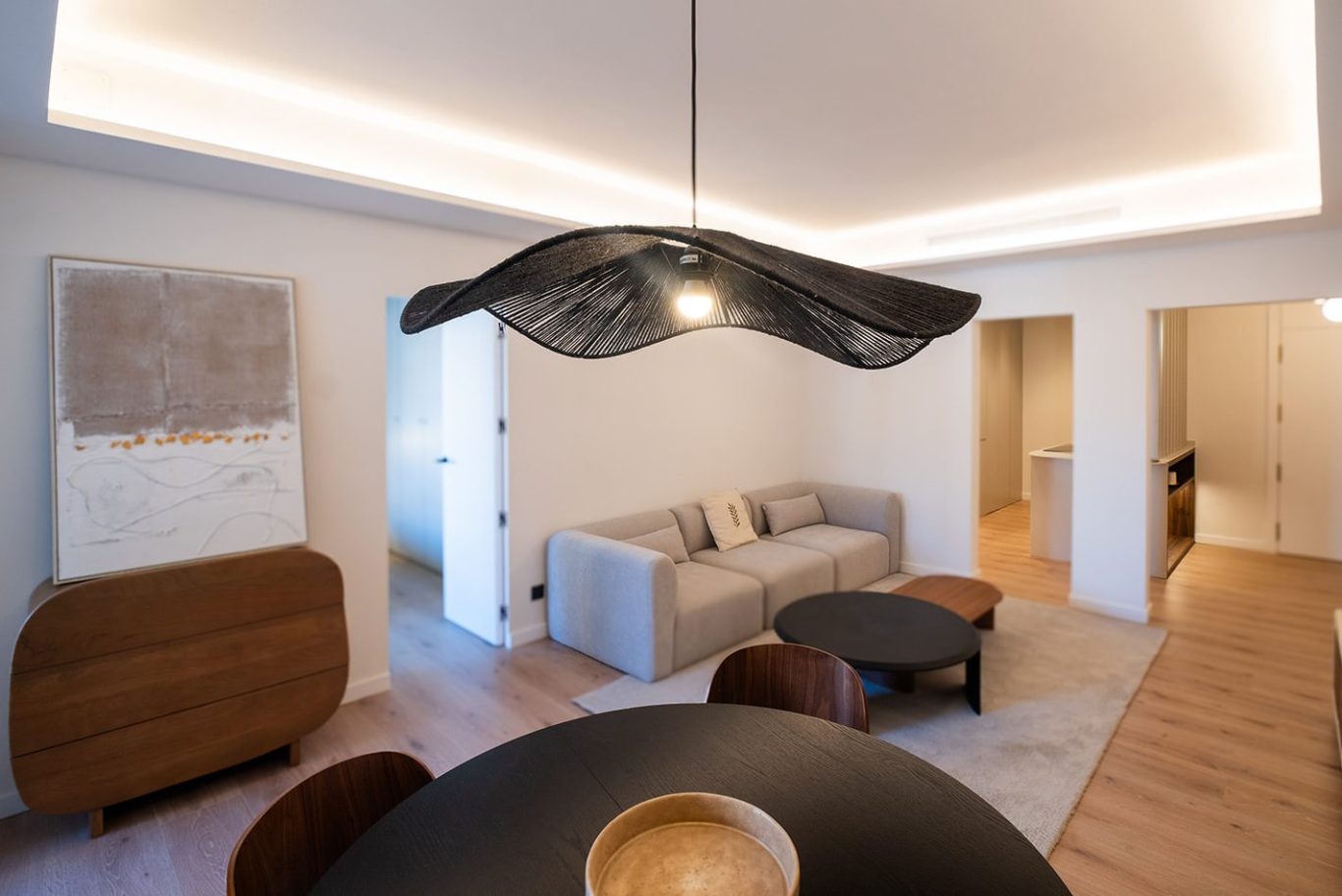 Salón moderno con sofá claro, mesa negra y una gran lámpara colgante. Paredes blancas.