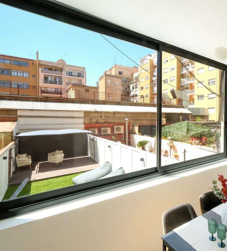 Vista interior de una vivienda con un jardín y edificios en el fondo.