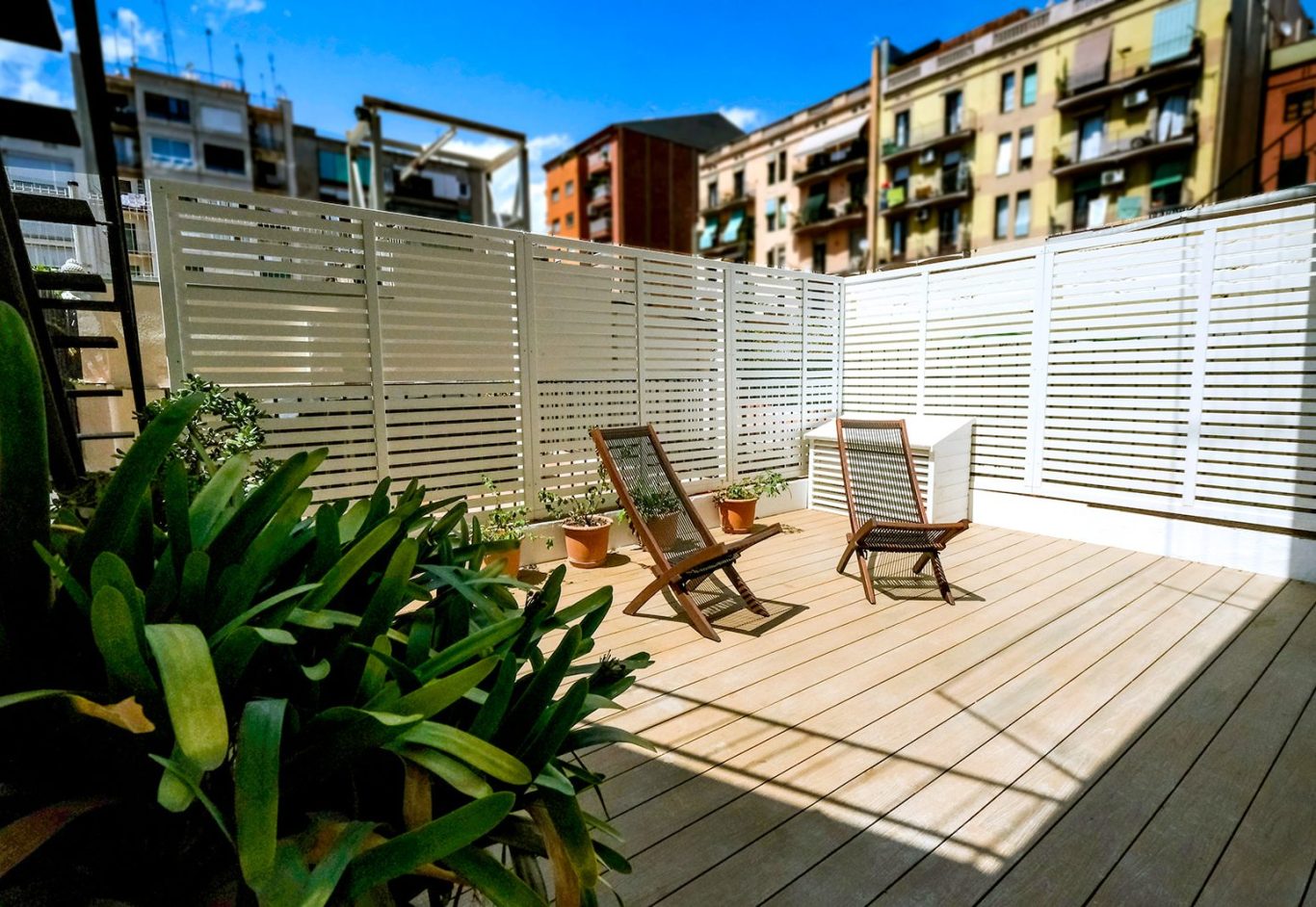 Terraza luminosa con dos sillas, mesa y plantas en un entorno urbano.