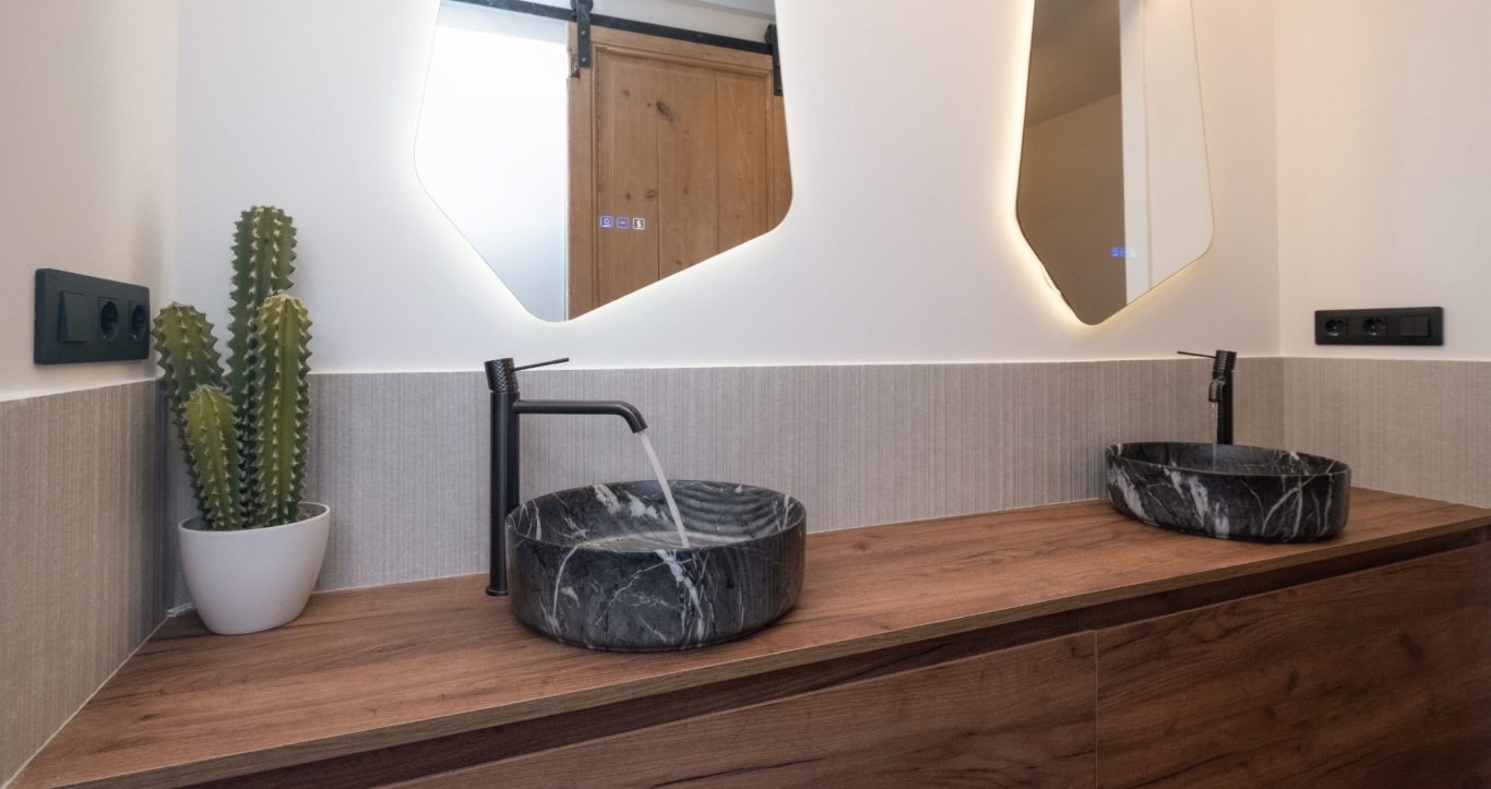 Dos lavabos de mármol negro sobre una encimera de madera, con cactus decorativo.