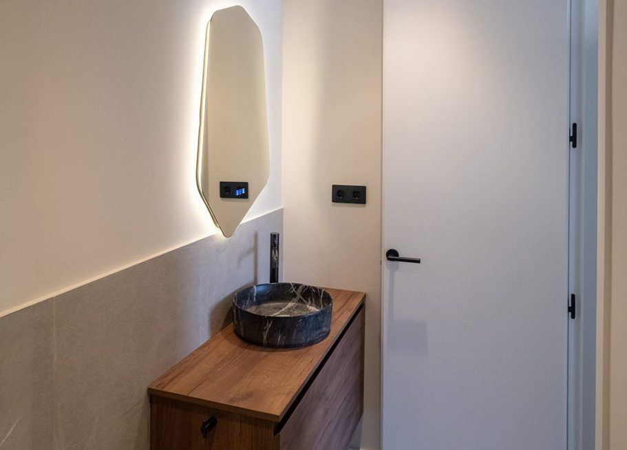 Baño moderno con lavabo sobre mueble de madera y espejo iluminado.
